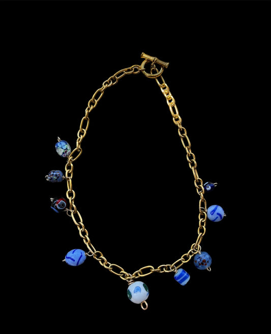 Handcrafted gold toggle clasp necklace adorned with an array of distinctive blue charms, each meticulously sourced and uniquely captivating.