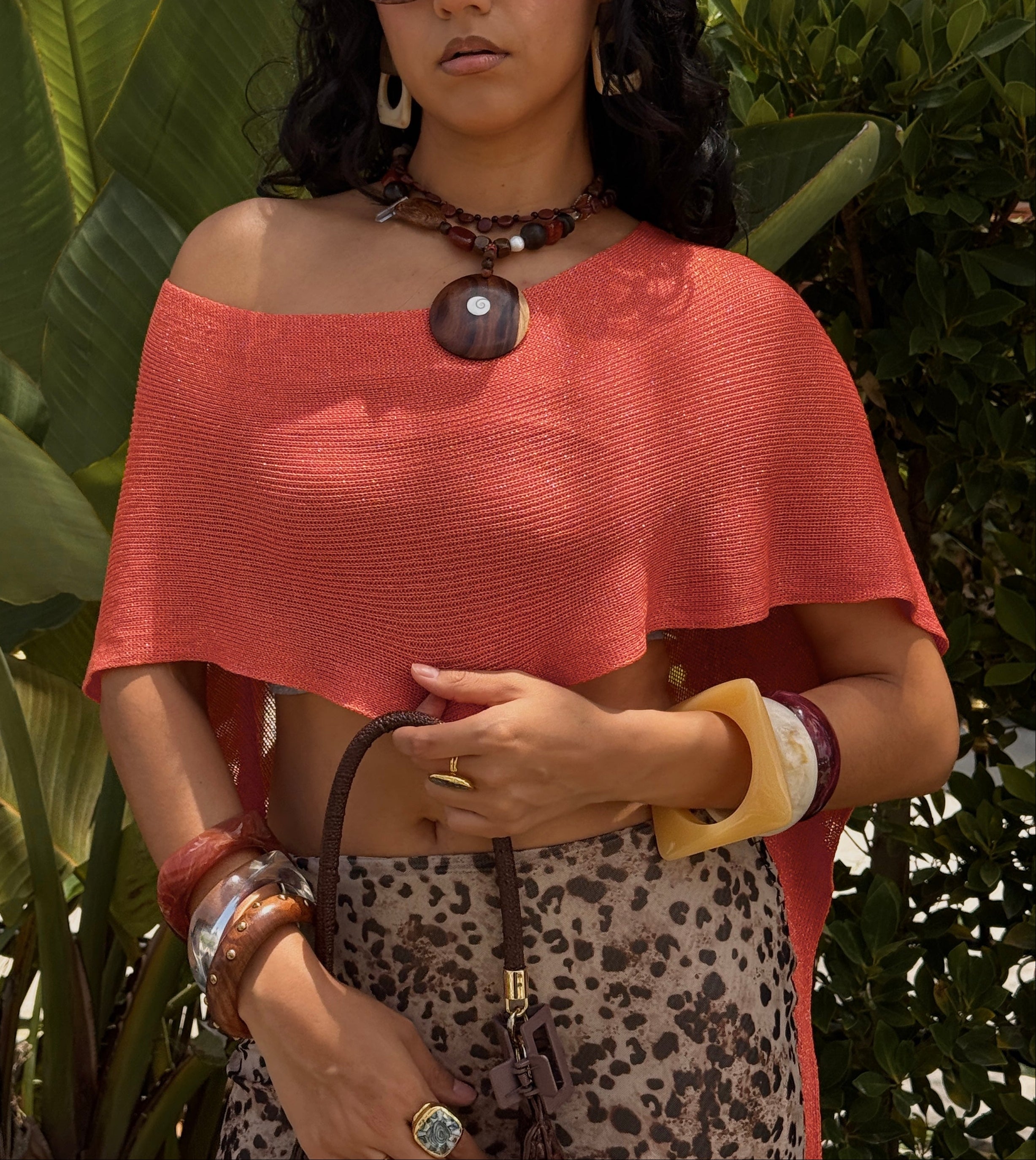 Woman wearing an orange top and leopard print skirt outdoors with plants and a building in the background